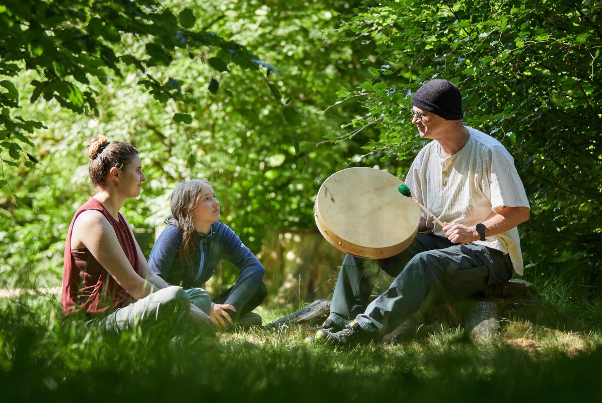 Mann mit Trommel und zwei Frauen im Wald