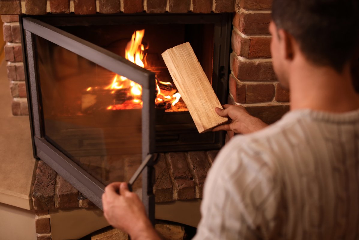 Mann heizt Feuer in einem offenen Kamin mit einem Scheitholz