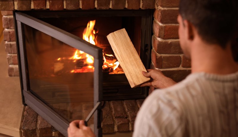 Mann heizt Feuer in einem offenen Kamin mit einem Scheitholz