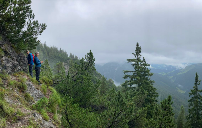Zwei Mitarbeiter stehen auf einer steilen Bergfläche mit Blick ins Tal