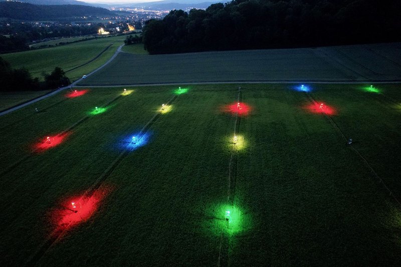nächtliche Flugaufnahme über einem Feld mit in 4 Farben leuchtenden Lichtquellen
