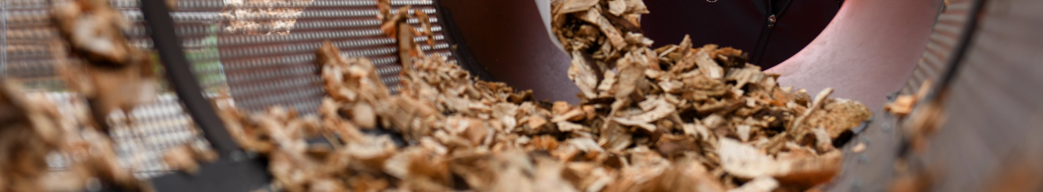 Frau siebt Hackschnitzel im Trommelsieb.