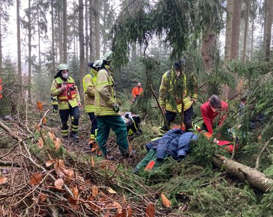 mehrere Rettungskräfte mitten im Wald bei der Bergung eines Verletzten