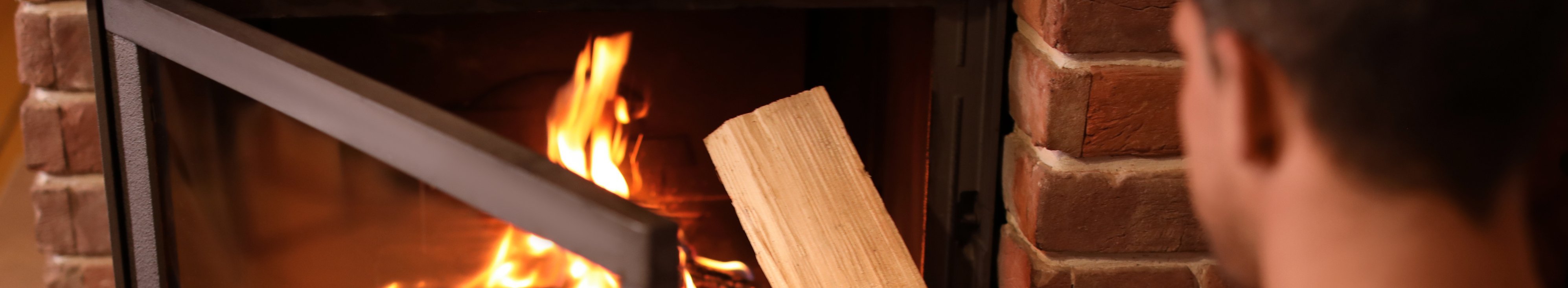 Mann heizt Feuer in einem offenen Kamin mit einem Scheitholz