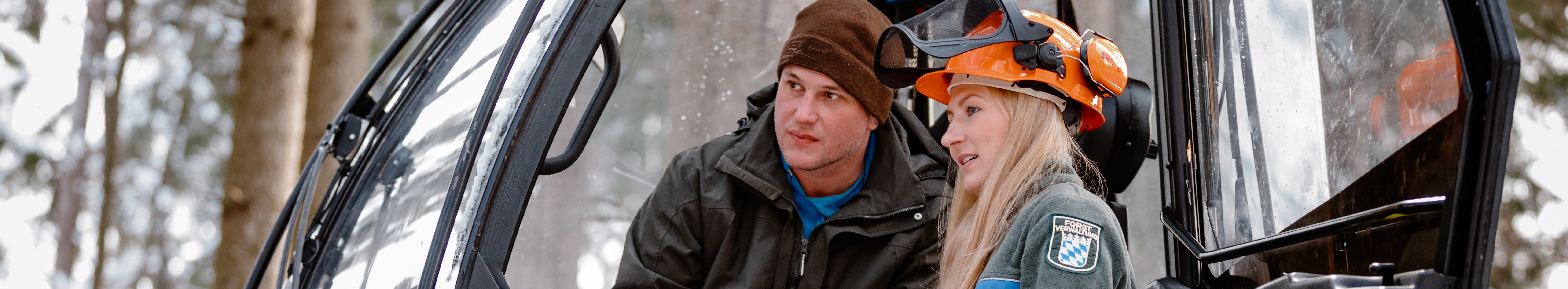 Försterin steht neben einer Harvester-Kanzel und gibt dem Fahrer Anweisungen