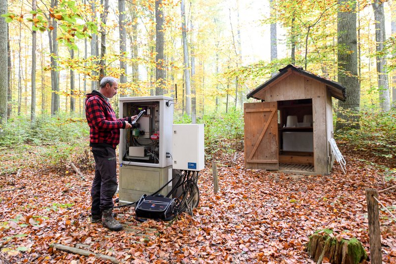 An employee in a red jacket is recording data from a digital measuring station using a laptop. 